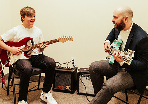 A boy playing guitar with music teacher
