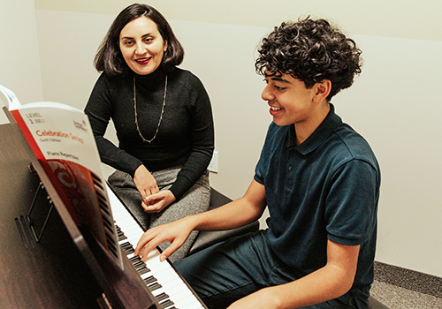 Piano teacher sitting next to boy playing piano