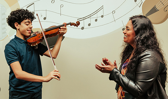 A boy playing violin while violin teacher claps